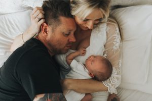 Image of a couple lying down while holding a baby taken by Melanie Grace