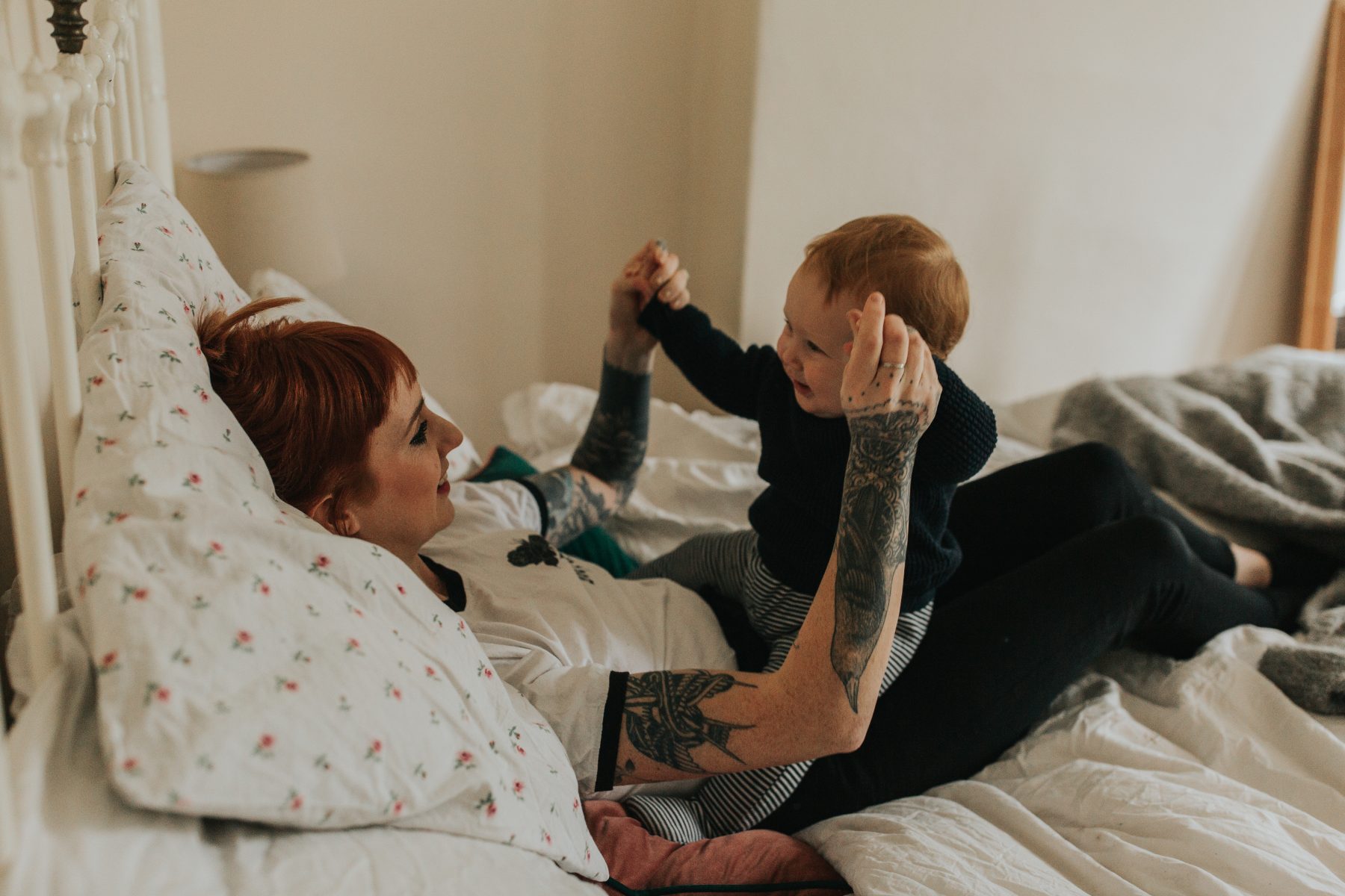 An image of a woman lying down playing with a smiling baby taken by Melanie Grace