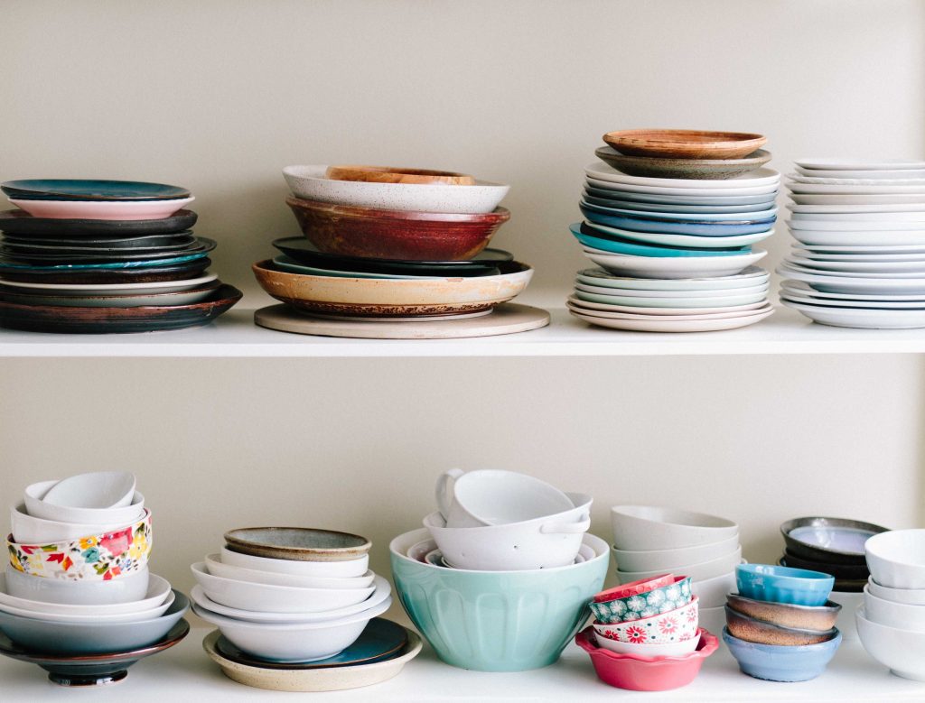 White shelves containing stacks of plates and bowls of different colours and sizes.