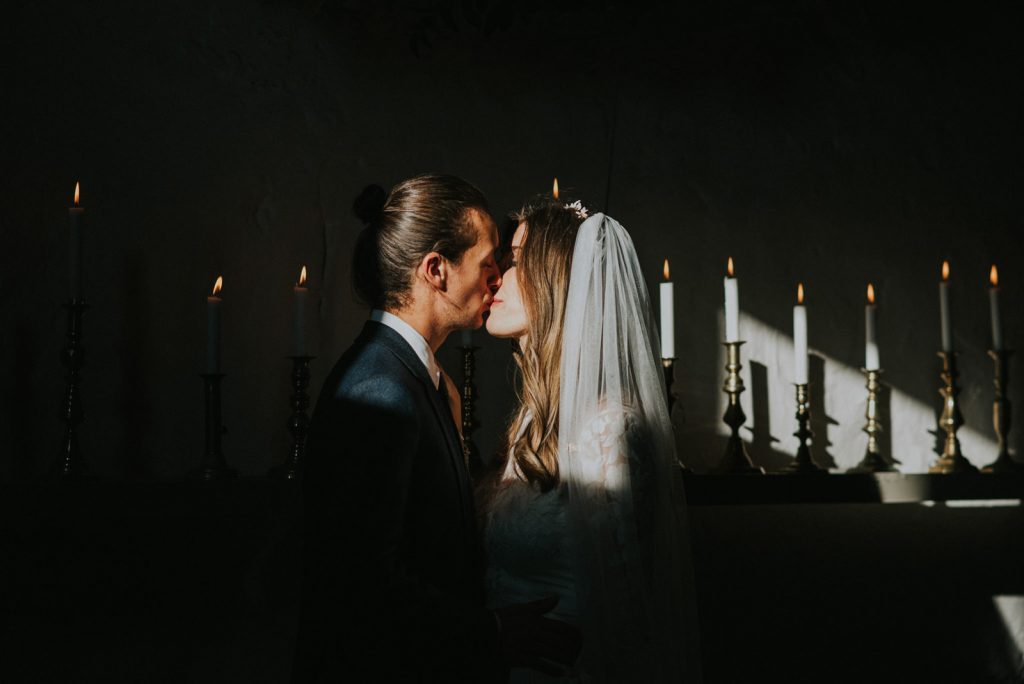 Image of a bride and groom kissing in a shadowy candle lit room taken by Fern Edwards